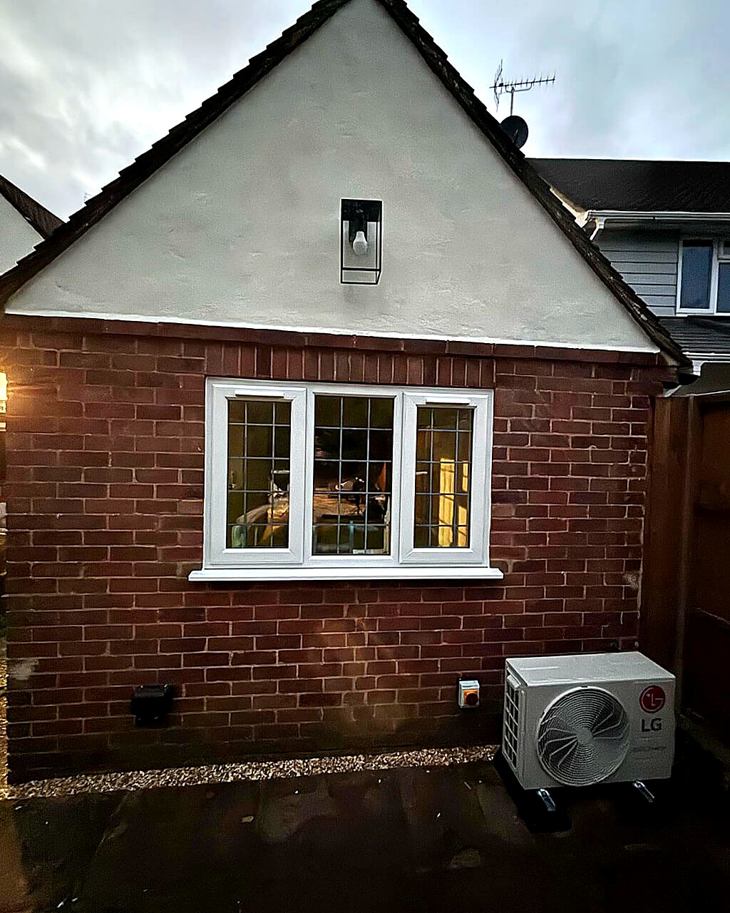 Gable end of a brick extension with a rendered gable and a leaded window, photographed at dusk