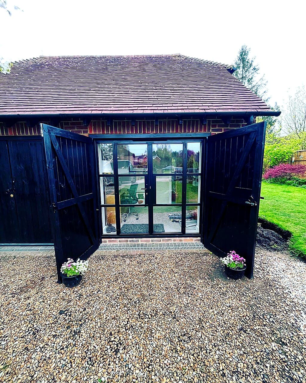 Brick garage converted into a garden office, with black timber barn doors opened onto glazed doors
